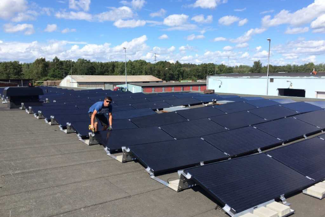 Montering av solceller där vi ser en solcellsmontör installera en solcellsanläggning på ett stort tak