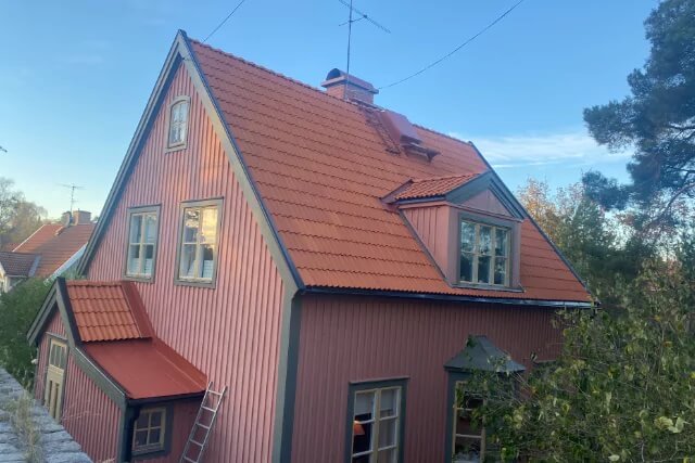 Ett rosa hus i Bromma där det genomförts en takrenovering med lite träd och blå himmel i bild